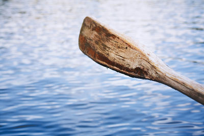 Close up of an old wooden paddle above blue water surface