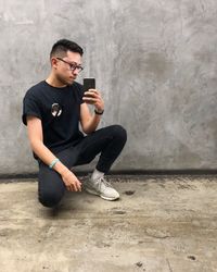 Young man using mobile phone while sitting on wall