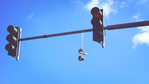 Low angle view of shoes hanging on road signal against blue sky