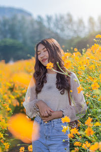 Smiling woman standing by yellow flowering plants
