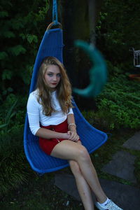 Portrait of woman sitting on swing against plants