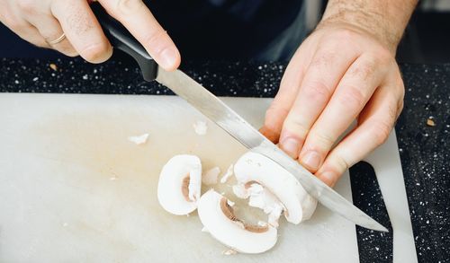 Close-up of man cutting edible mushroom on cutting board in kitchen