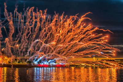 Firework display over lake against sky at night