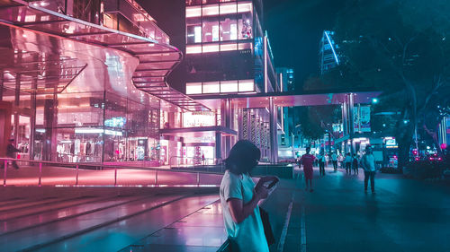 Woman standing on illuminated street in city at night