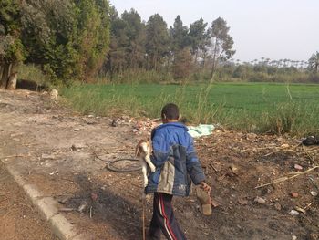 Rear view of boy carrying kid goat walking on field