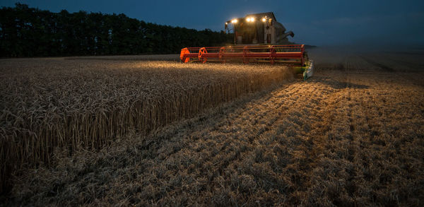 Low angle view of combine harvester against sky during dusk