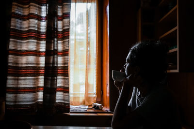 Side view of woman drinking tea while sitting at home