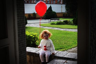 Girl in spooky costume holding red balloon seen through doorway