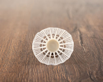 Rear view of the plumage of a white plastic badminton shuttlecock on a wooden background.