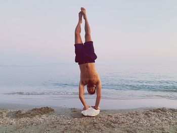 Full length of shirtless man doing handstand at beach against sky