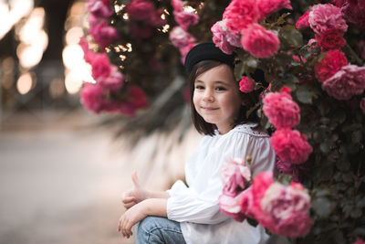 Portrait of young kid girl sitting over pink rose flowers in garden outdoor