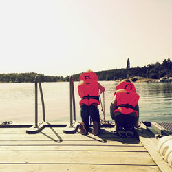 Full length of men sitting on lake against clear sky