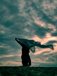 Low angle view of man with arms raised standing against sky during sunset