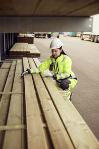 Female worker in protective workwear arranging planks at lumber industry