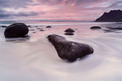 Rocks on beach against sky during sunset