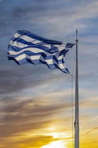 The greek flag against dramatic beautiful sunset and clouds, moving with the wind .