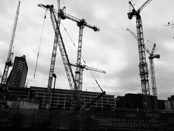 Low angle view of cranes at construction site against sky