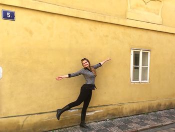 Full length portrait of young woman standing against building in city
