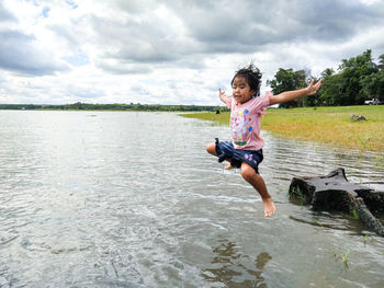 Full length of girl jumping in lake against sky