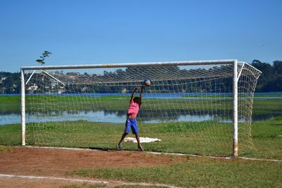 Boy playing soccer on field against clear sky