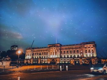 Illuminated building by street against sky at night