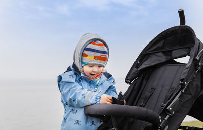 Cute girl standing by baby stroller against sky