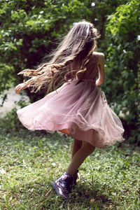 Baby girl with long hair in a purple dress and boots whirls around herself standing on the ground 