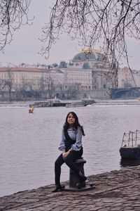 Portrait of young woman sitting by river in city