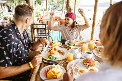 Happy girl clenching fists while parents having breakfast at table in resort