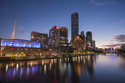 Illuminated buildings by river against sky at night