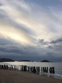 Wooden posts on beach against sky during sunset