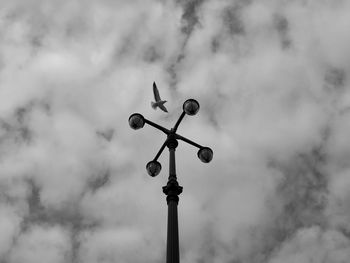 Low angle view of bird flying over street light against cloudy sky