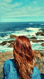 Rear view of woman sitting at beach against sky