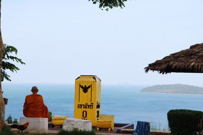 Rear view of man sitting by sea against clear sky