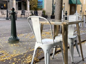 Empty chairs and tables on sidewalk cafe by street in city