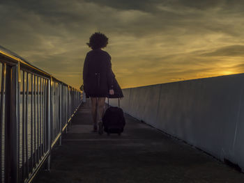 Rear view of woman standing on railing against sky