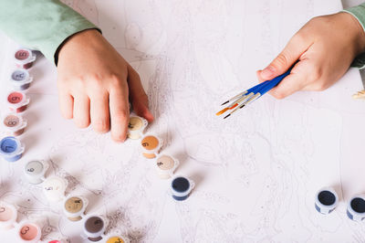 Girl's hands holding brushes and paints for painting by numbers