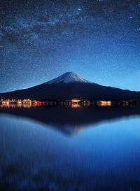 Distant view of volcanic mountain with reflection on lake against star field at night