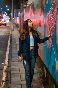 Young woman looking at painted wall at night