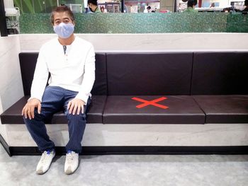 Full length portrait of young man sitting on wall