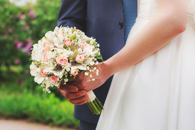 Midsection of wedding couple holding bouquet