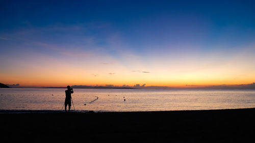 Silhouette person standing on beach against sky during sunset