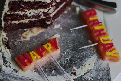 Colorful happy birthday greeting candles. slice of red velvet cake on a white plate