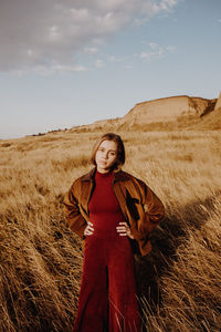 Portrait of young woman standing on field against sky