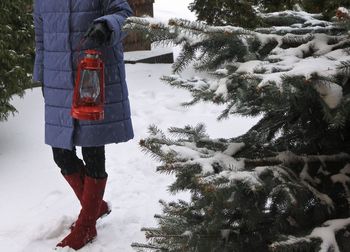 Low section of woman with lantern walking on snowy field