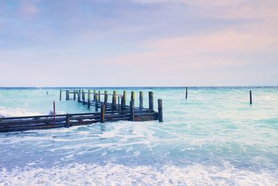 Abandoned wooden wharf in sea within blue pink color of sky, blur waves on water level.