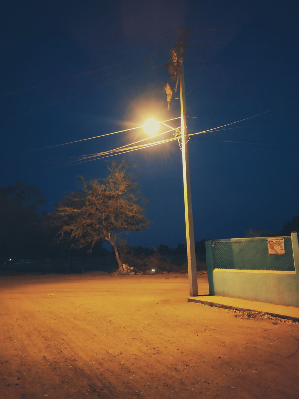 ILLUMINATED STREET LIGHT ON FIELD AGAINST SKY