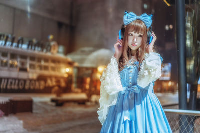 Beautiful young woman wearing headphones standing at night