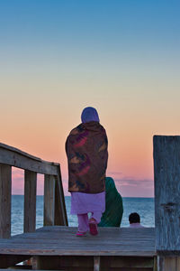 Rear view of people looking at sea against sky during sunset