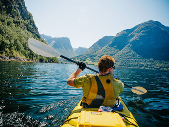 Rear view of man with umbrella on river against mountains